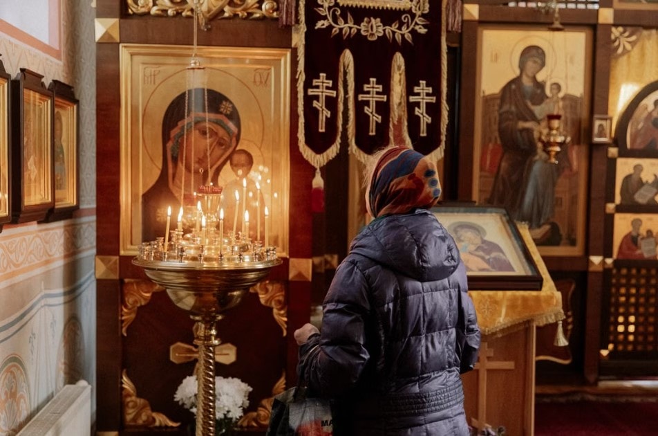 A woman in prayer before candles in a church, reflecting discernment of consecrated life